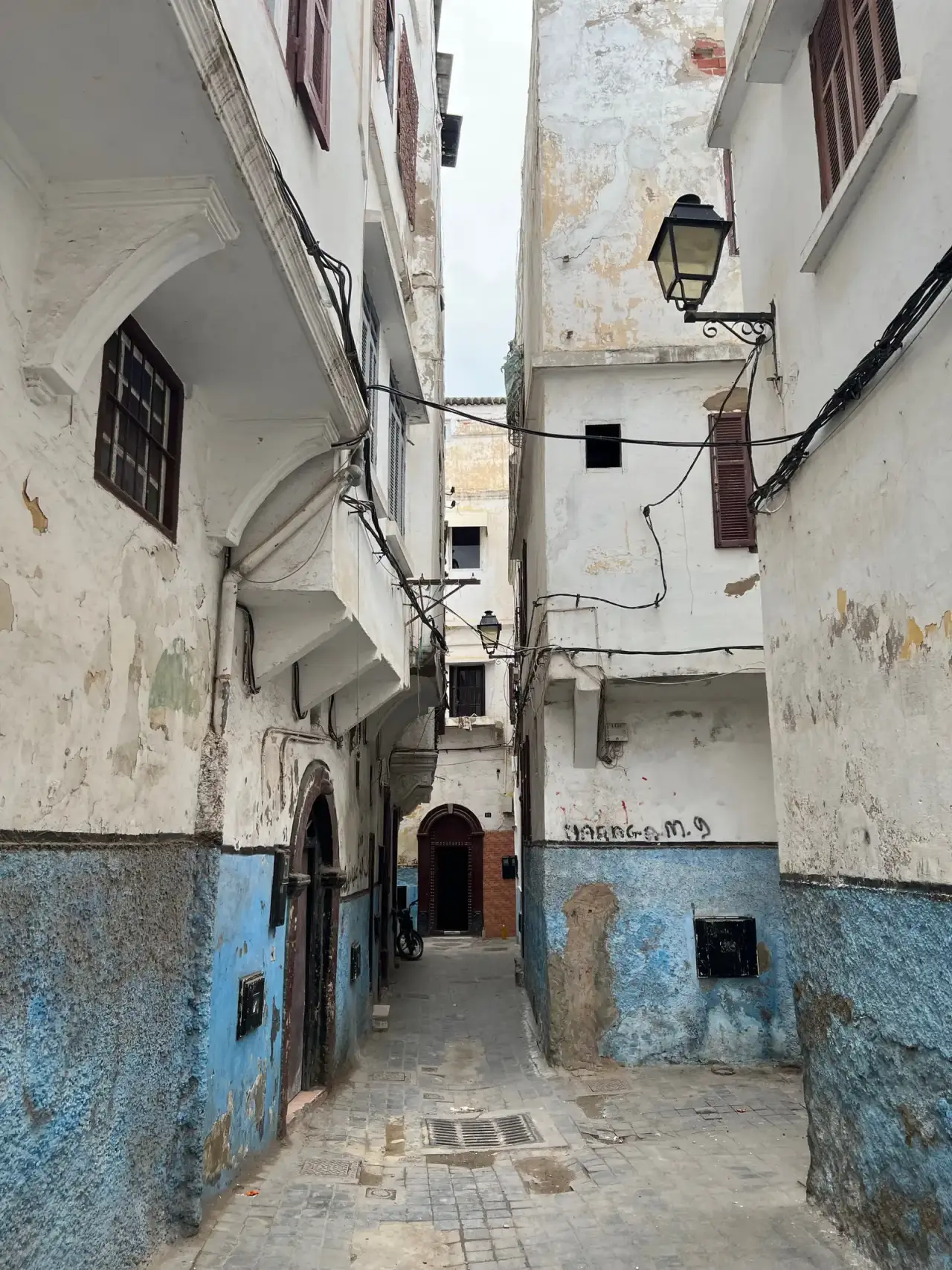 Ruelle étroite aux murs clairs, avec des câbles tirés entre les façades.
